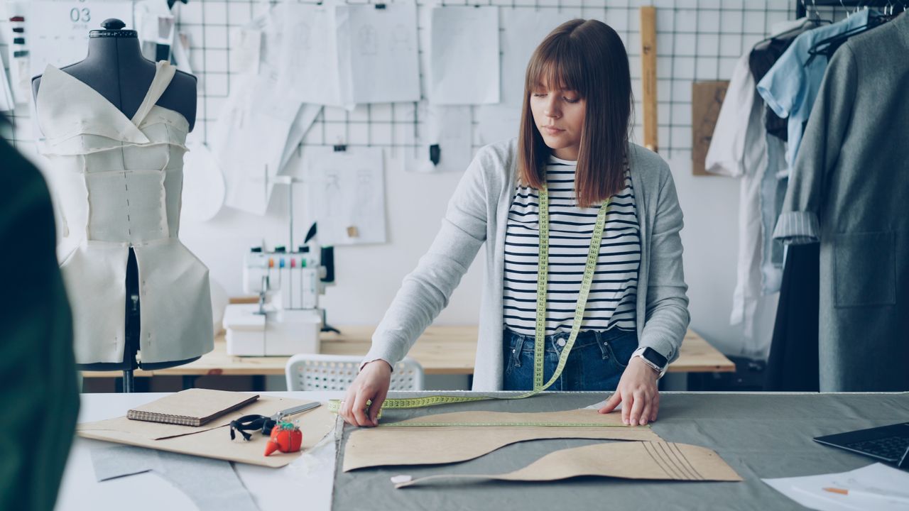 Young woman fashion designer measuring fabric in studio with tailoring tools.