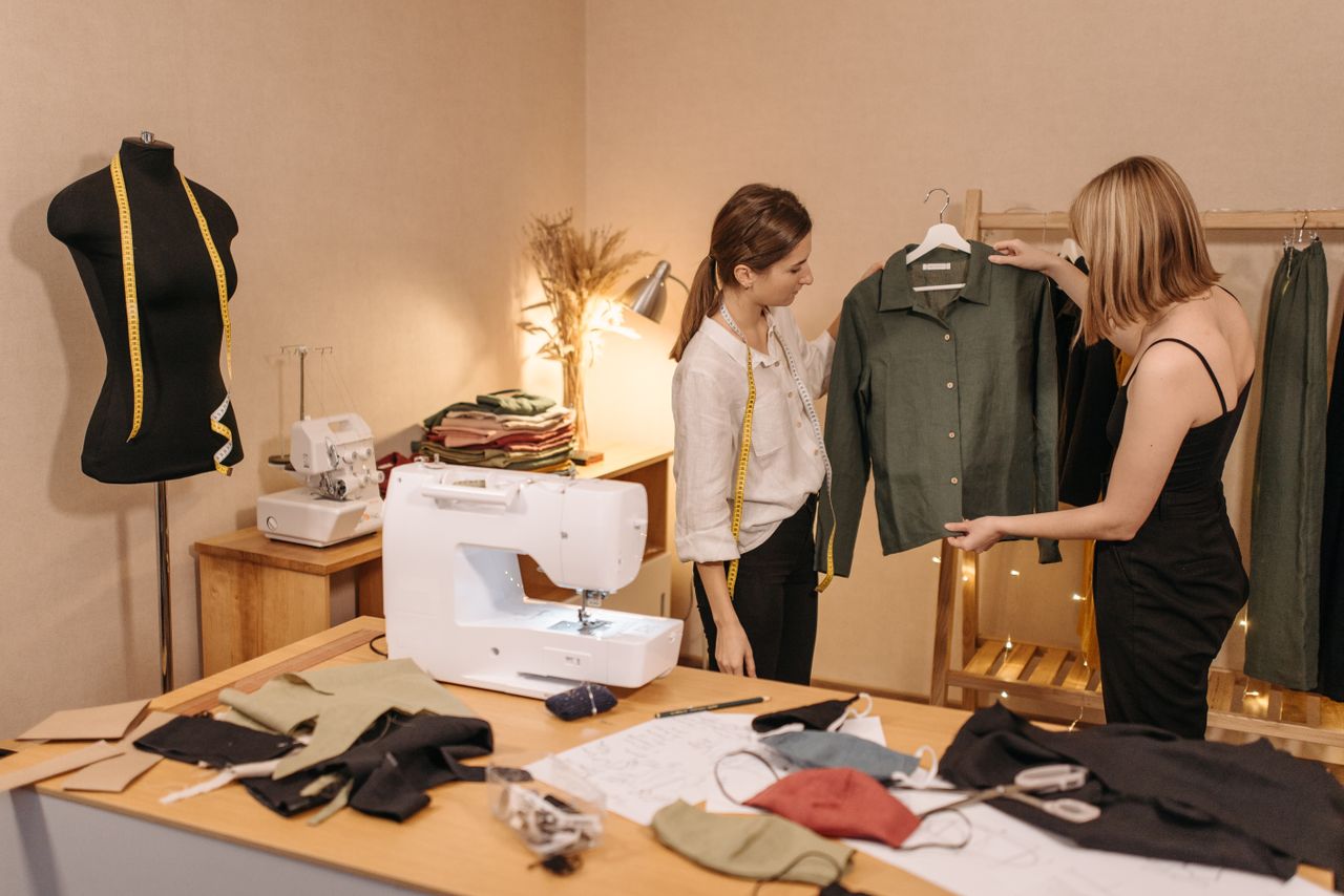 Home Two women working together in a sewing studio, examining a handcrafted green shirt.